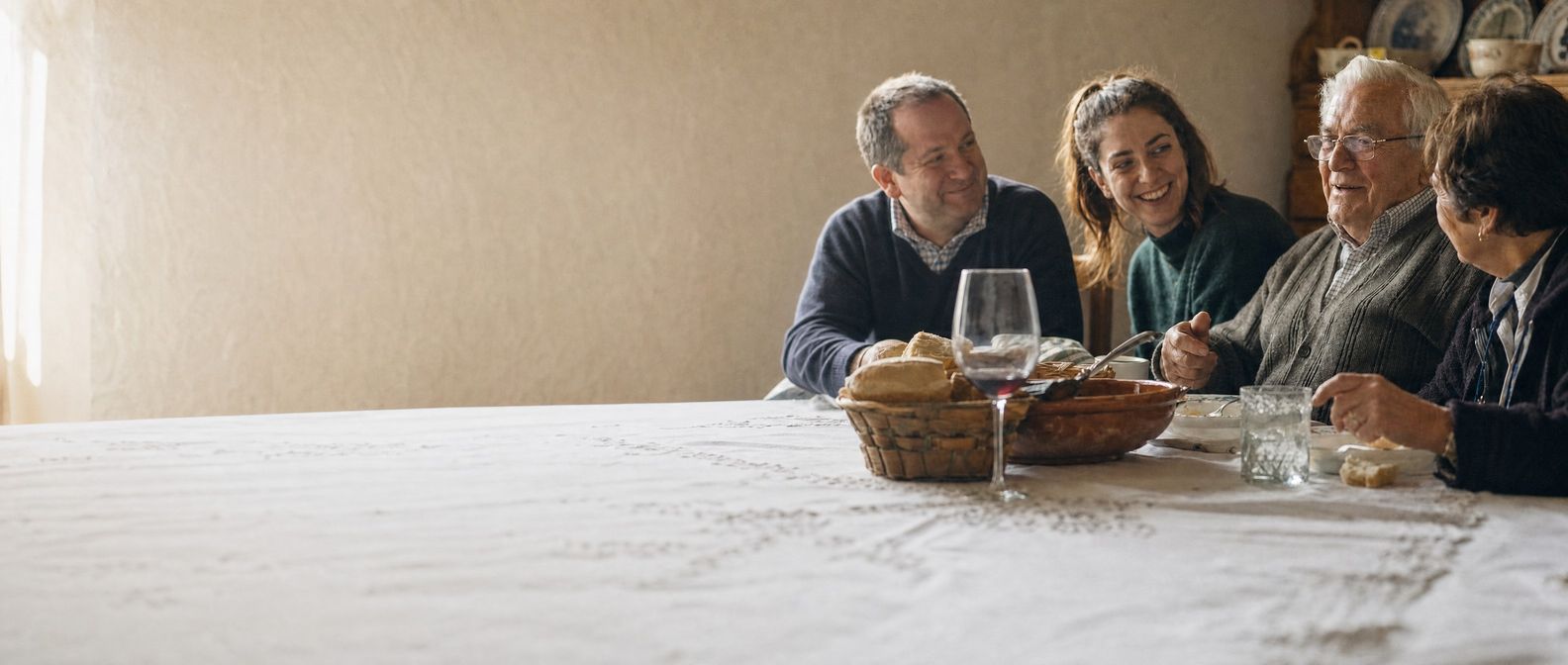 A family Sunday lunch: an older man at the head of the table follows the conversation while his family talks.